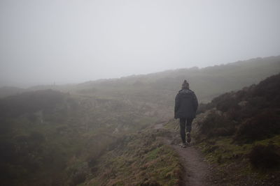 Rear view of man walking on mountain against sky