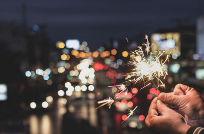 Cropped hands of person holding illuminated sparkler at night