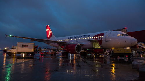 Airplane on wet airport runway against sky at dusk