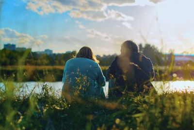 Rear view of couple sitting at lakeshore against sky