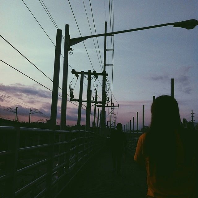 silhouette, power line, sky, electricity pylon, connection, cable, men, sunset, power supply, electricity, low angle view, built structure, lifestyles, transportation, technology, cloud - sky, person, architecture, dusk