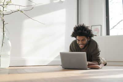 Smiling man lying on floor in empty room with laptop