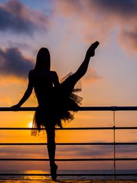 Silhouette woman dancing by railing against sea during sunset