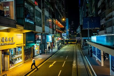 People walking on illuminated road amidst buildings at night
