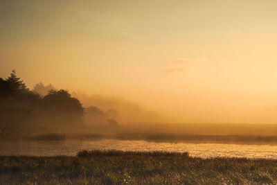 Scenic view of lake against sky during sunset at foggy weather