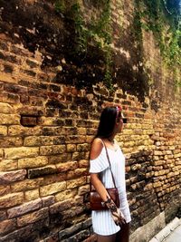 Rear view of young woman standing against brick wall