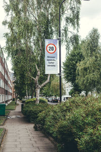 Road sign by trees on footpath in city