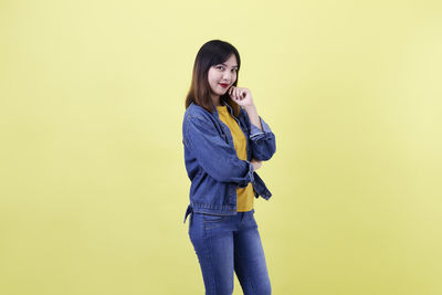 Young woman using phone while standing against yellow background
