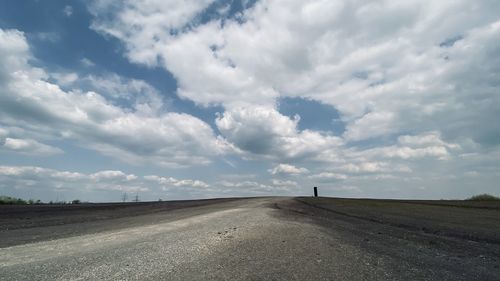 Empty road amidst field against sky