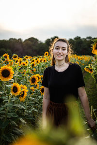 Portrait of smiling woman standing by sunflower plants against sky