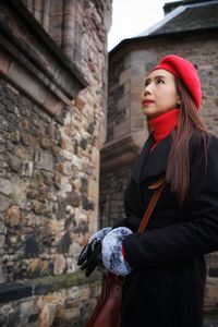 Young woman looking away while standing against brick wall