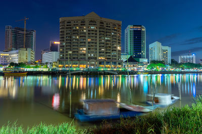 Illuminated buildings by river against sky at night