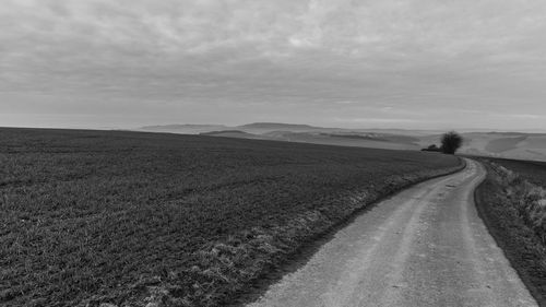 Dirt road amidst field against sky