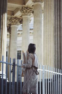 Rear view of woman holding baguette while standing fence