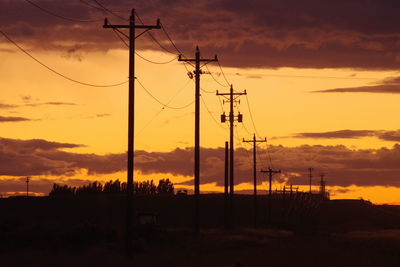 Silhouette electricity pylons on land against sky during sunset