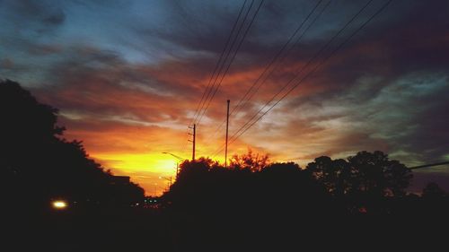 Low angle view of silhouette electricity pylon against dramatic sky