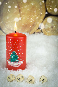 Close-up of red lit candle by toy bocks text during christmas