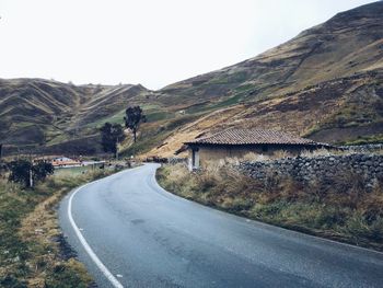 Country road leading towards mountains against clear sky