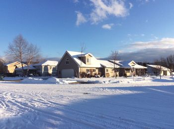 Snow covered field by houses against sky