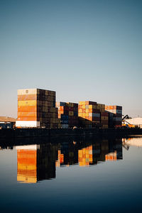 Reflection of containers in canal against clear sky