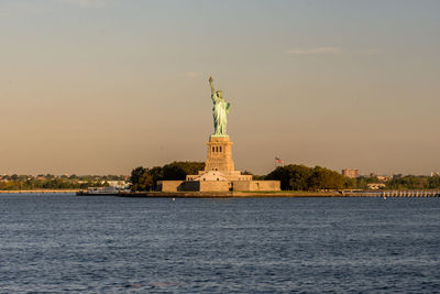 Statue of liberty at sea against sky during sunset