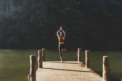 Rear view of woman in tree pose over pier