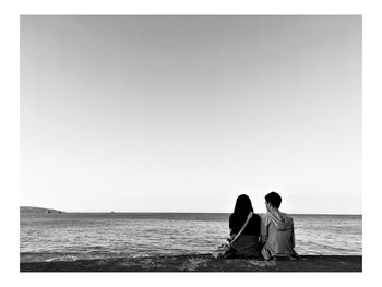 Rear view of friends looking at sea against clear sky