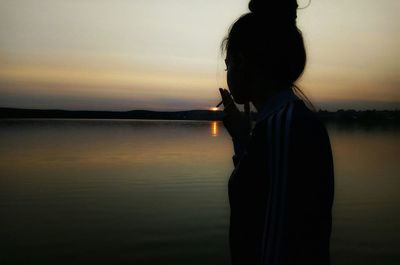 Silhouette woman standing by lake against sky during sunset