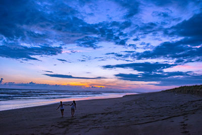 People on beach against sky during sunset