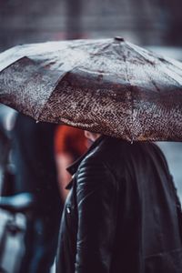 Midsection of woman carrying umbrella while walking on street during monsoon