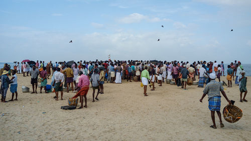 Fishermen gathered at beach against sky