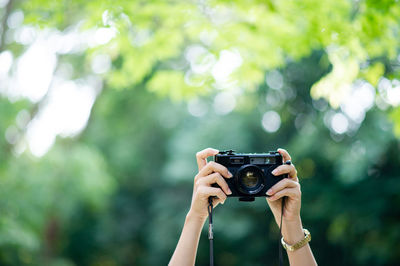 Cropped hand of woman holding camera against plants