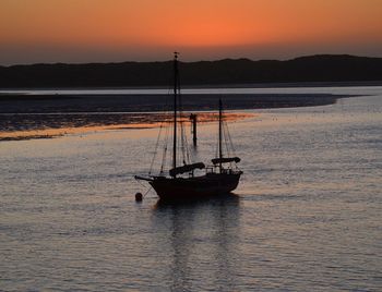 Silhouette sailboat in calm sea at sunset