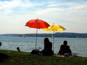 People sitting on sea shore against sky