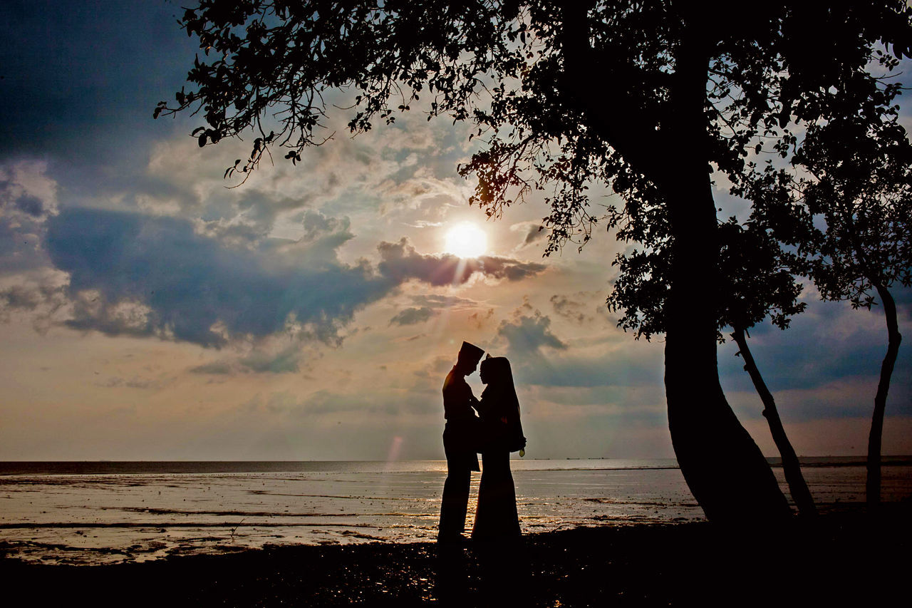 SILHOUETTE MAN STANDING ON SHORE AGAINST SUNSET SKY