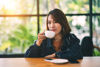 Woman drinking coffee while sitting by table in cafe