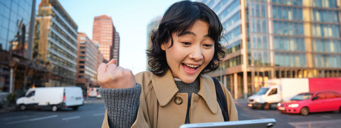 Portrait of young woman standing against city