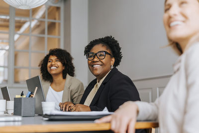 Smiling businesswoman with colleagues sitting and discussing in meeting room at office