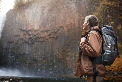 Male hiker carrying backpack while looking at waterfall