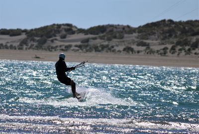 Side view of man kiteboarding on sea during sunny day