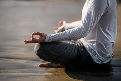 Low section of man meditating while sitting at beach