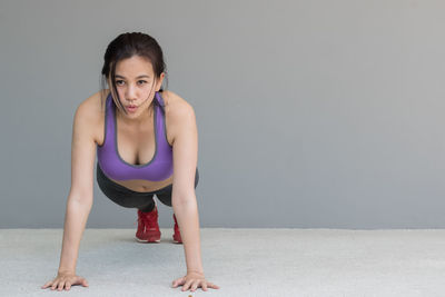 Full length of woman doing push-ups against wall