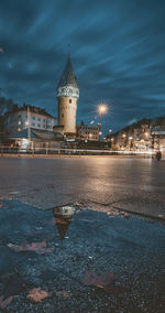 Illuminated building by river against sky at dusk