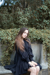 Young woman smiling while sitting on plant against trees