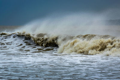 Sea waves splashing on shore against sky