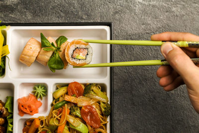 Cropped image of hand holding sushi with chopsticks in plate