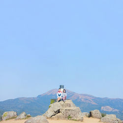 Man sitting on mountain against clear blue sky