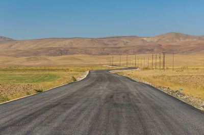 Country road leading towards mountains against blue sky