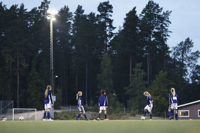 Surface level view of girls practicing soccer on field against trees