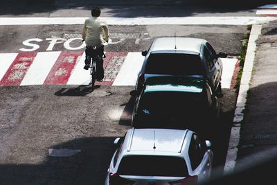 Rear view of man riding bicycle on street by cars